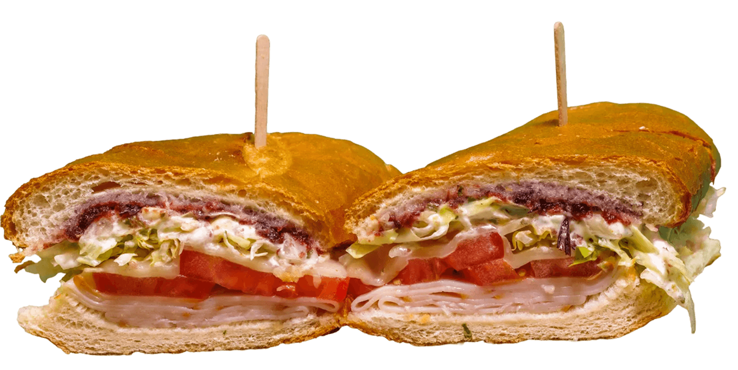 A large turkey breast submarine sandwich, cut in half and held by two wooden picks, reveals layers of sliced turkey, tomatoes, lettuce, creamy sauce, and a dark berry spread on a golden baguette.