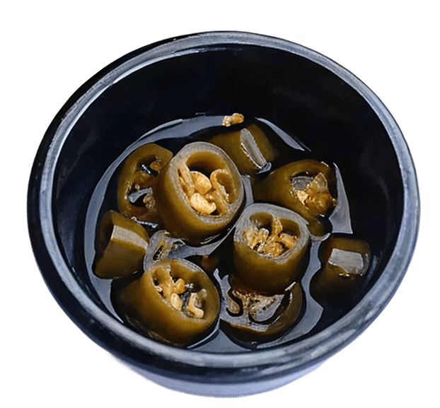 A black bowl of sliced pickled green jalapeño peppers submerged in a dark liquid, with visible seeds.