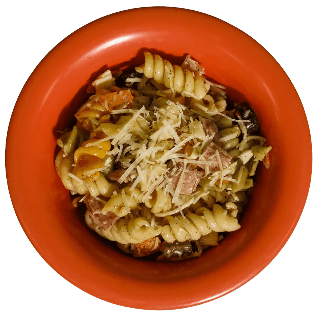 A top-down view of an orange bowl filled with fusilli pasta salad, garnished with shredded cheese, sliced ham, and diced vegetables.